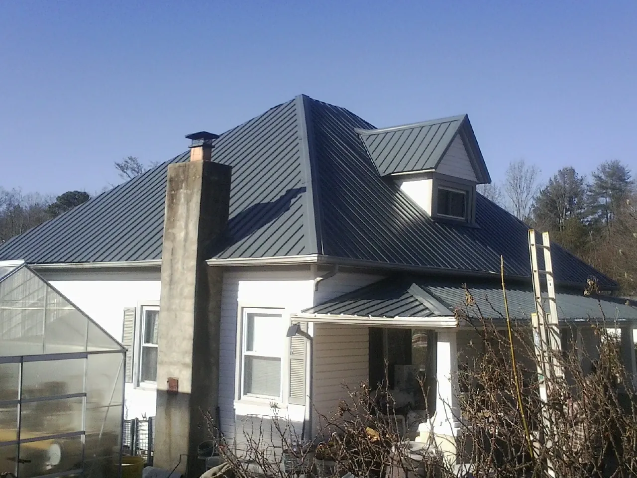 Dark blue standing seam metal roof on a white farmhouse with dormer — Slate & Tile Roof Repair by Roofing Brothers in Amma