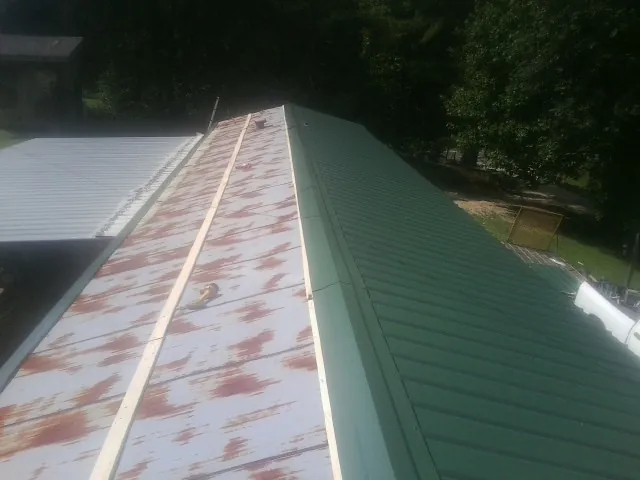 Old rusted panels beside newly installed green metal roofing — Wind Damage Roof Repair by Roofing Brothers in Amma