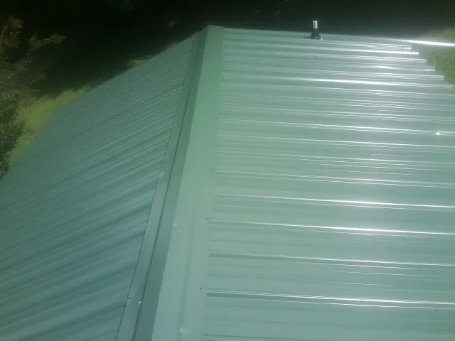 New green metal panels meeting at the ridge of a roof — Flat Roof Repair work by our crew in Amma
