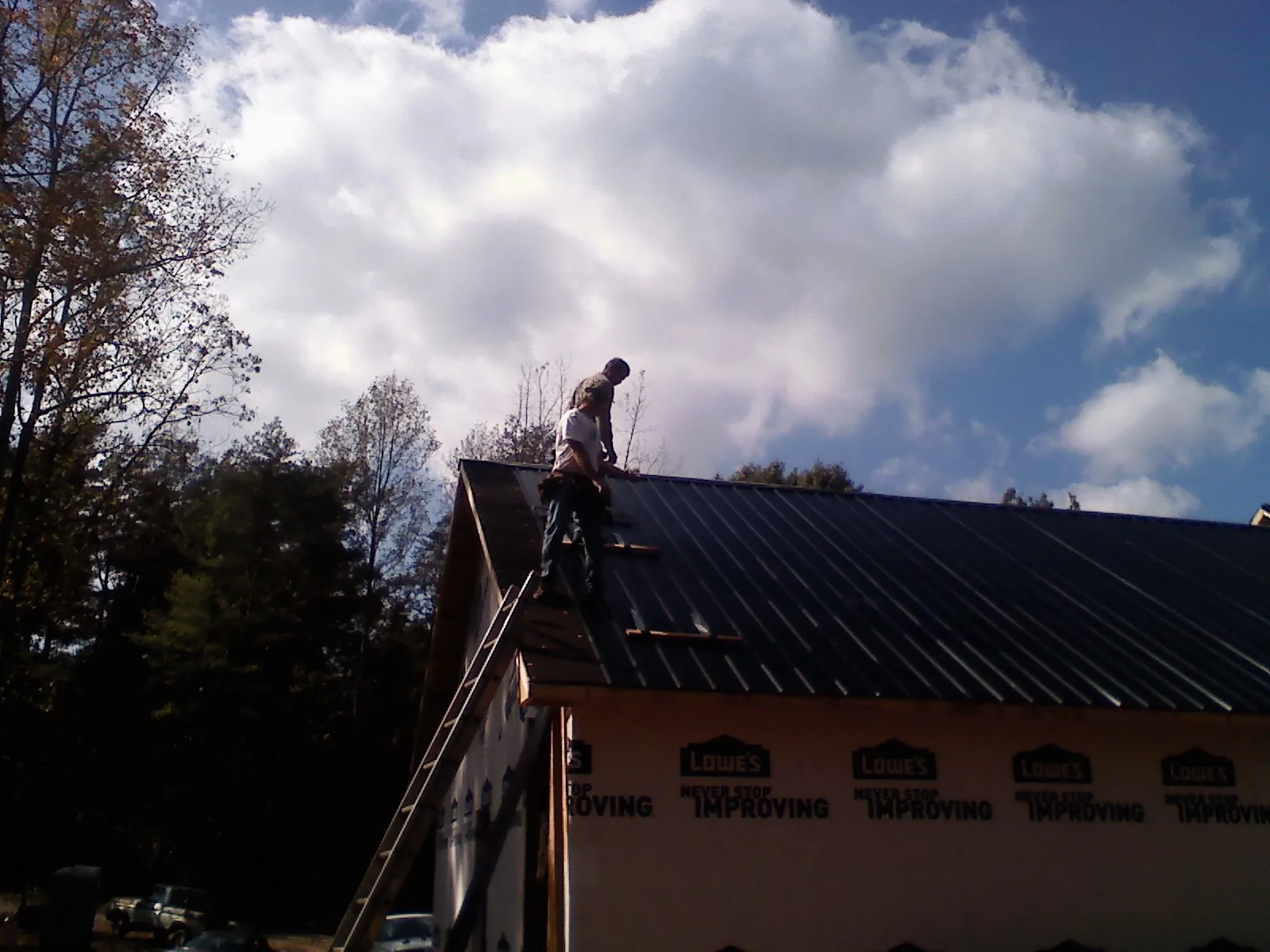 Roofer fastening dark metal panels high against a cloudy sky, from a Roof Inspection job in Amma