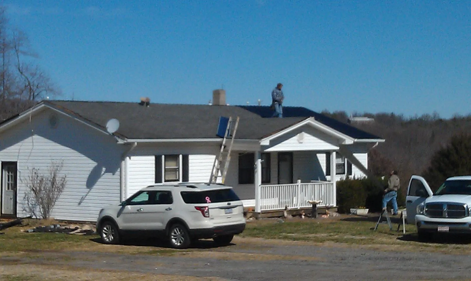Roofers stripping shingles from a white ranch house roof in Amma